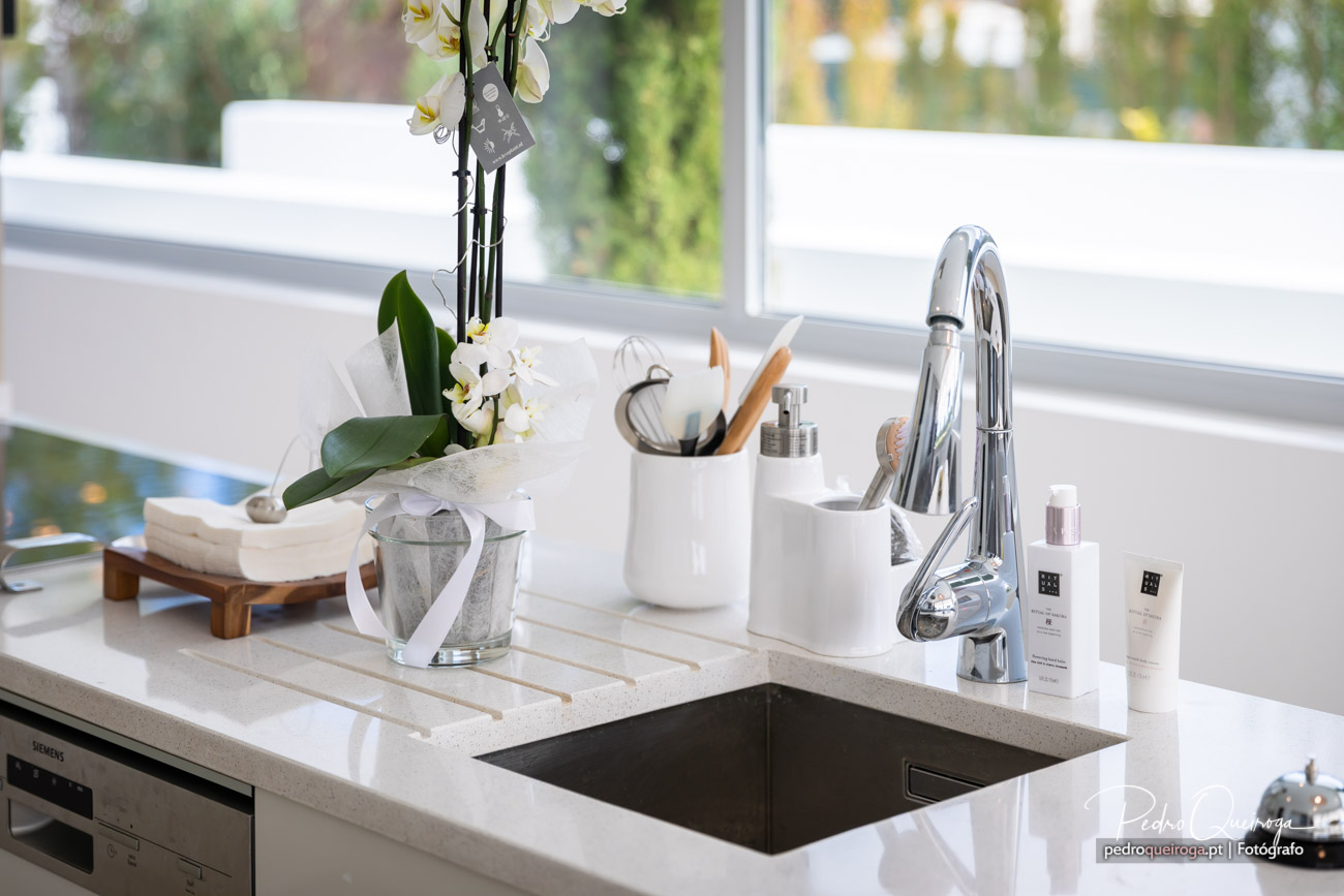 Bancada de cozinha moderna com orquídea branca, torneira cromada e utensílios organizados junto à janela iluminada