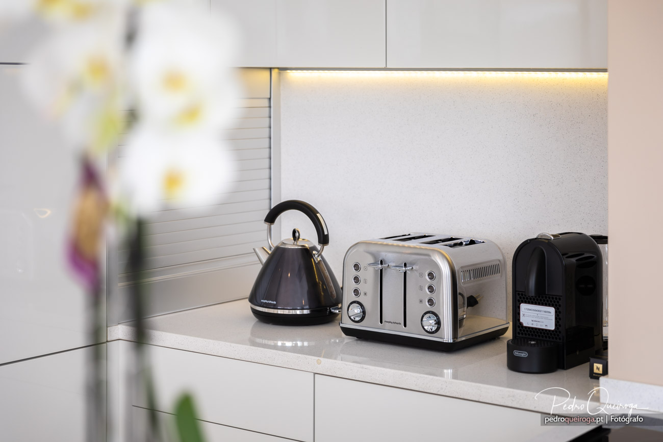 Bancada de cozinha moderna com chaleira, torradeira e máquina de café sobre superfície clara com iluminação LED