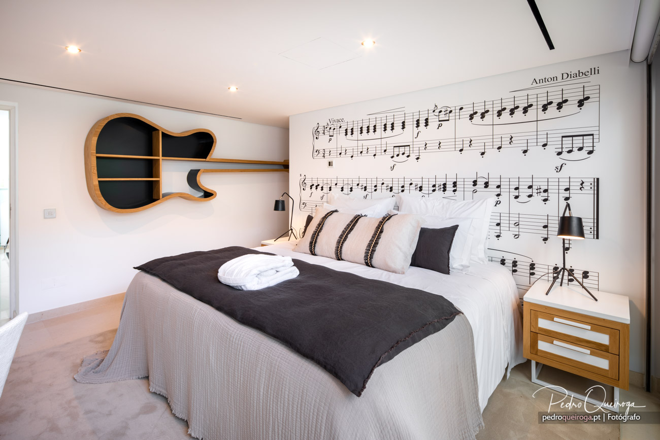 Quarto moderno com prateleira em forma de guitarra e papel de parede com partitura musical na cabeceira da cama