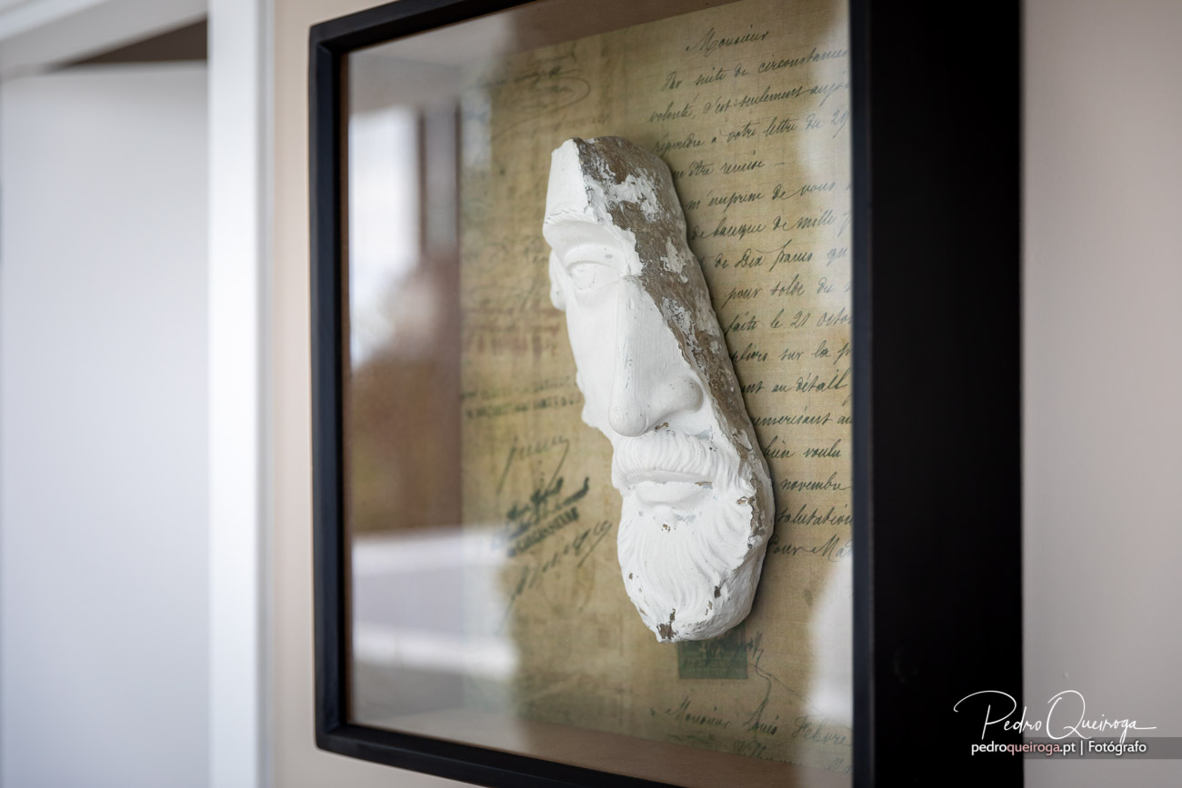 Máscara branca emoldurada sobre manuscrito antigo, captada por Pedro Queiroga com detalhe e profundidade artística