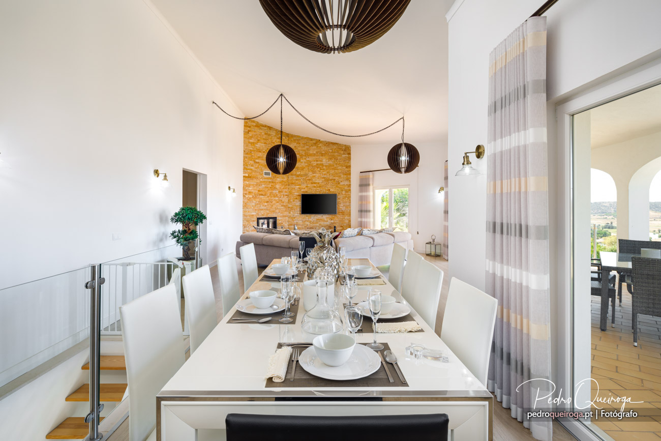 Sala de jantar ampla com mesa posta, parede em tijolo à vista e luminárias pendentes decorativas sobre pé-direito alto