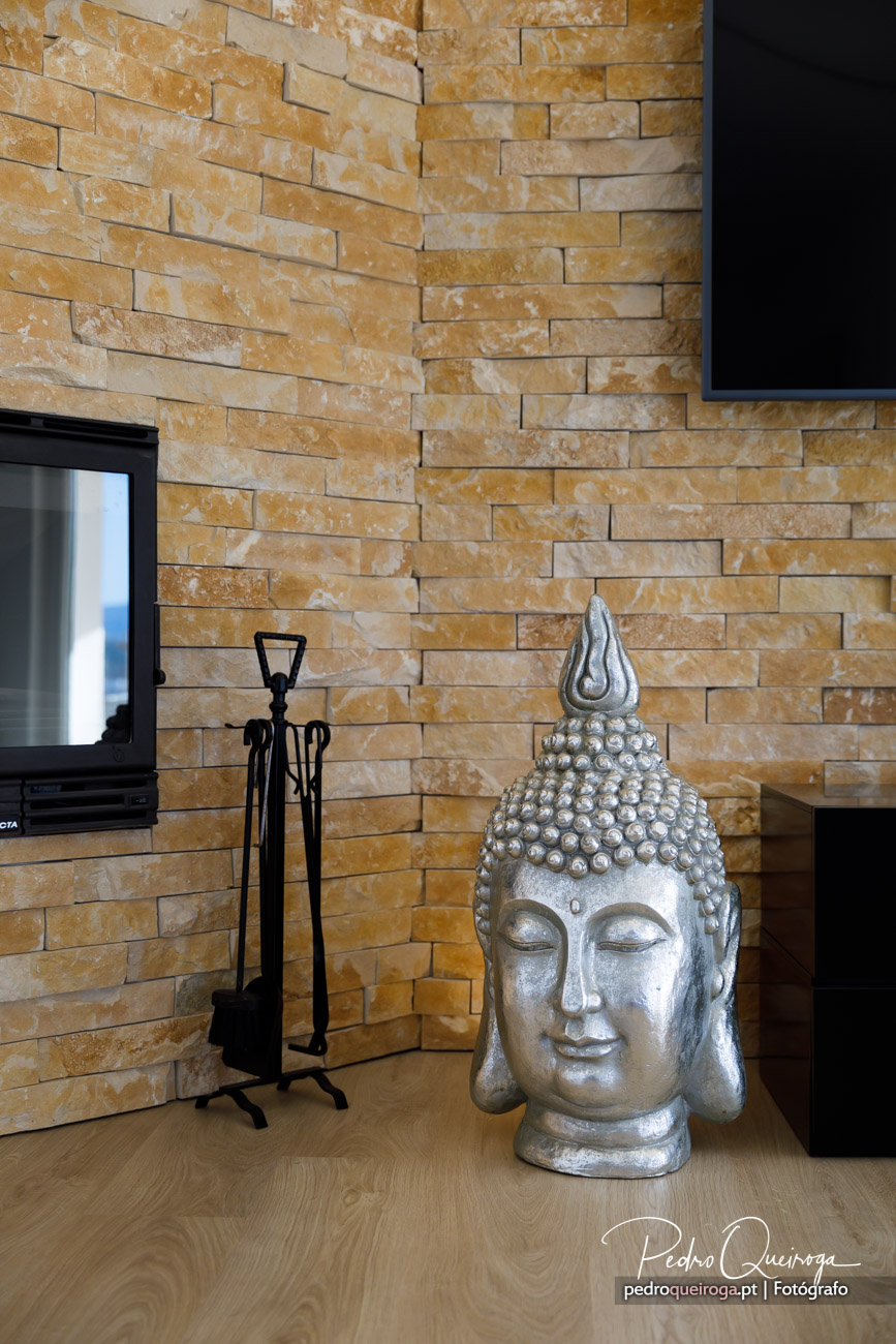 Escultura decorativa de Buda prateada junto a lareira com revestimento em pedra natural por Pedro Queiroga