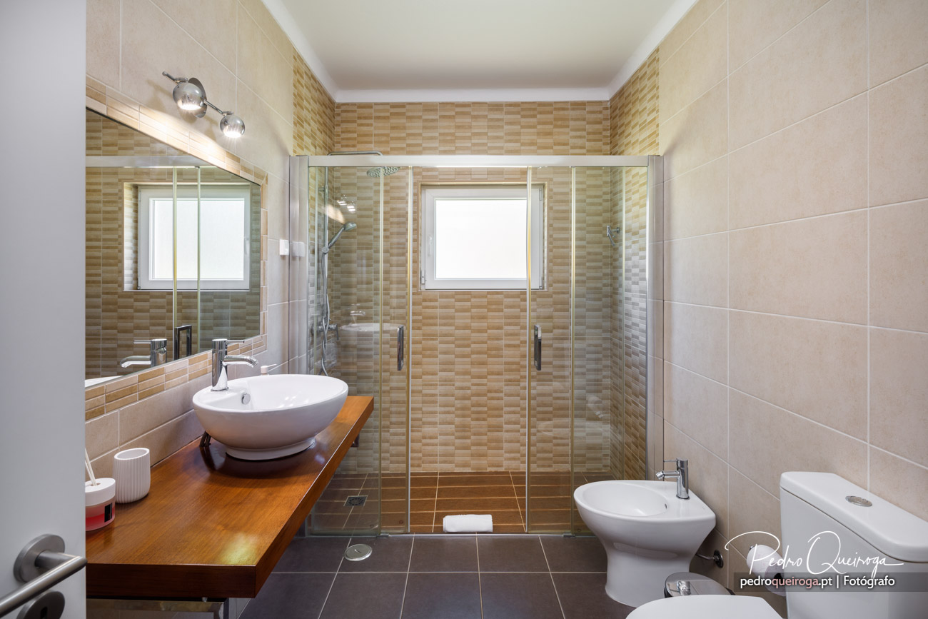 Casa de banho moderna com base de duche, lavatório sobre bancada em madeira e mosaico bege nas paredes.