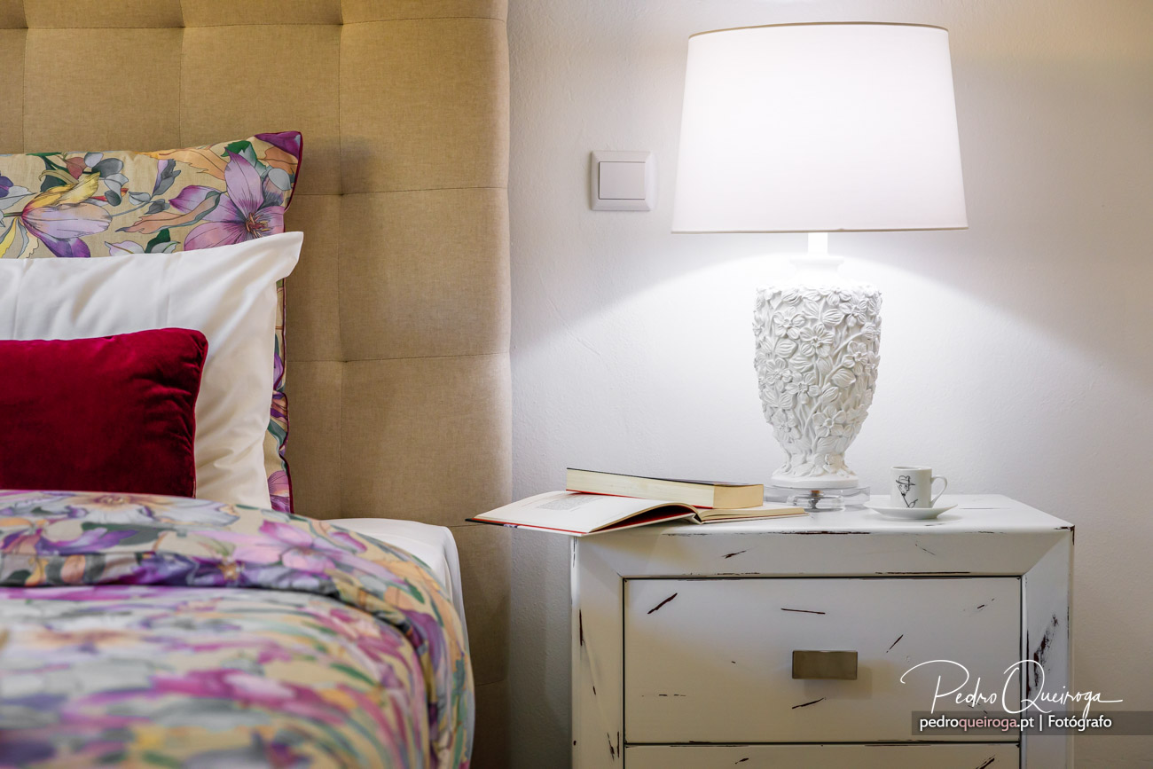 Quarto acolhedor com mesinha de cabeceira vintage branca, candeeiro decorativo e roupa de cama floral colorida