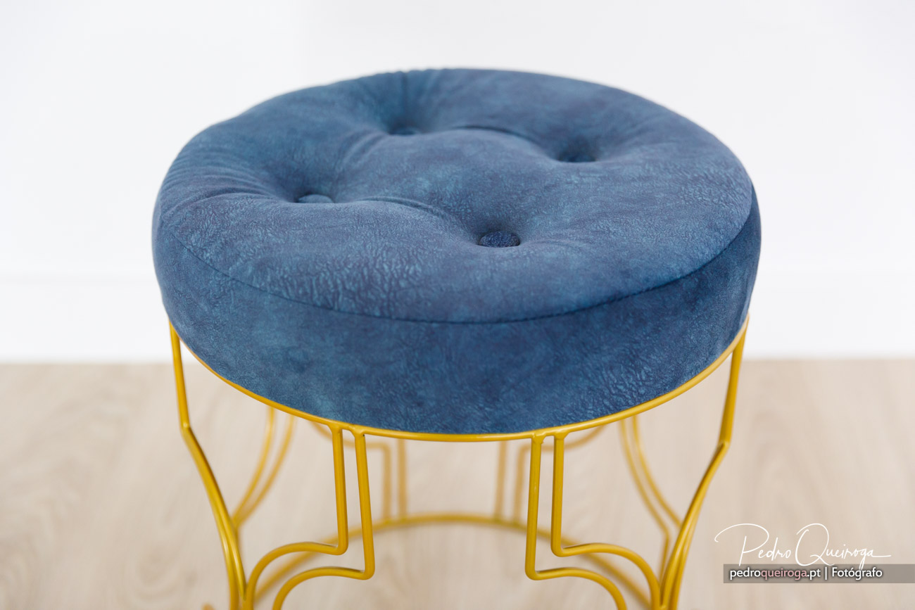 Puff redondo capitoné em veludo azul com estrutura metálica dourada sobre fundo neutro e minimalista