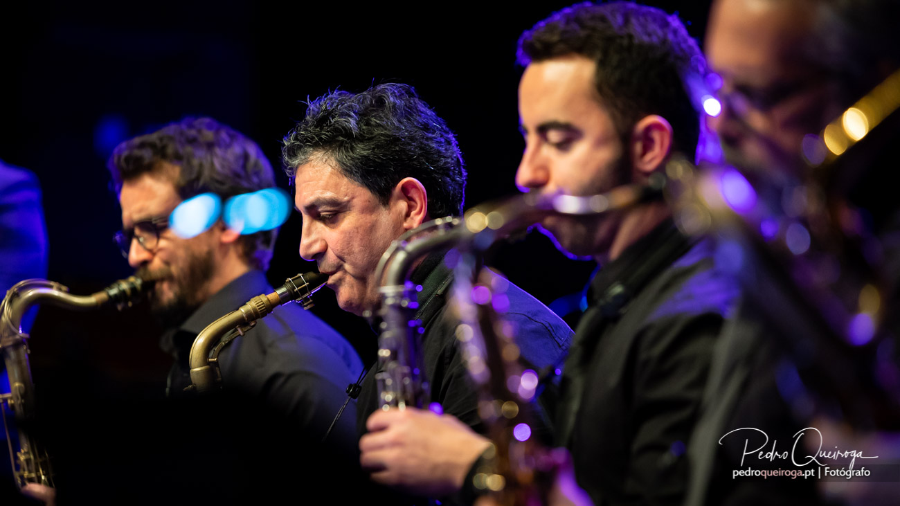 Saxofonistas concentrados durante atuação ao vivo com iluminação azul e roxa no palco