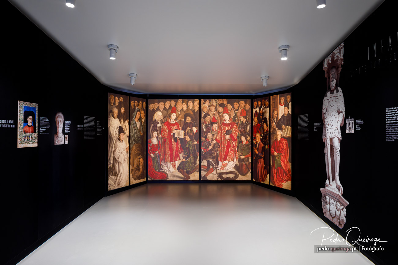 Sala de museu com paredes negras, decoração minimalista e painéis renascentistas iluminados ao centro e escultura lateral