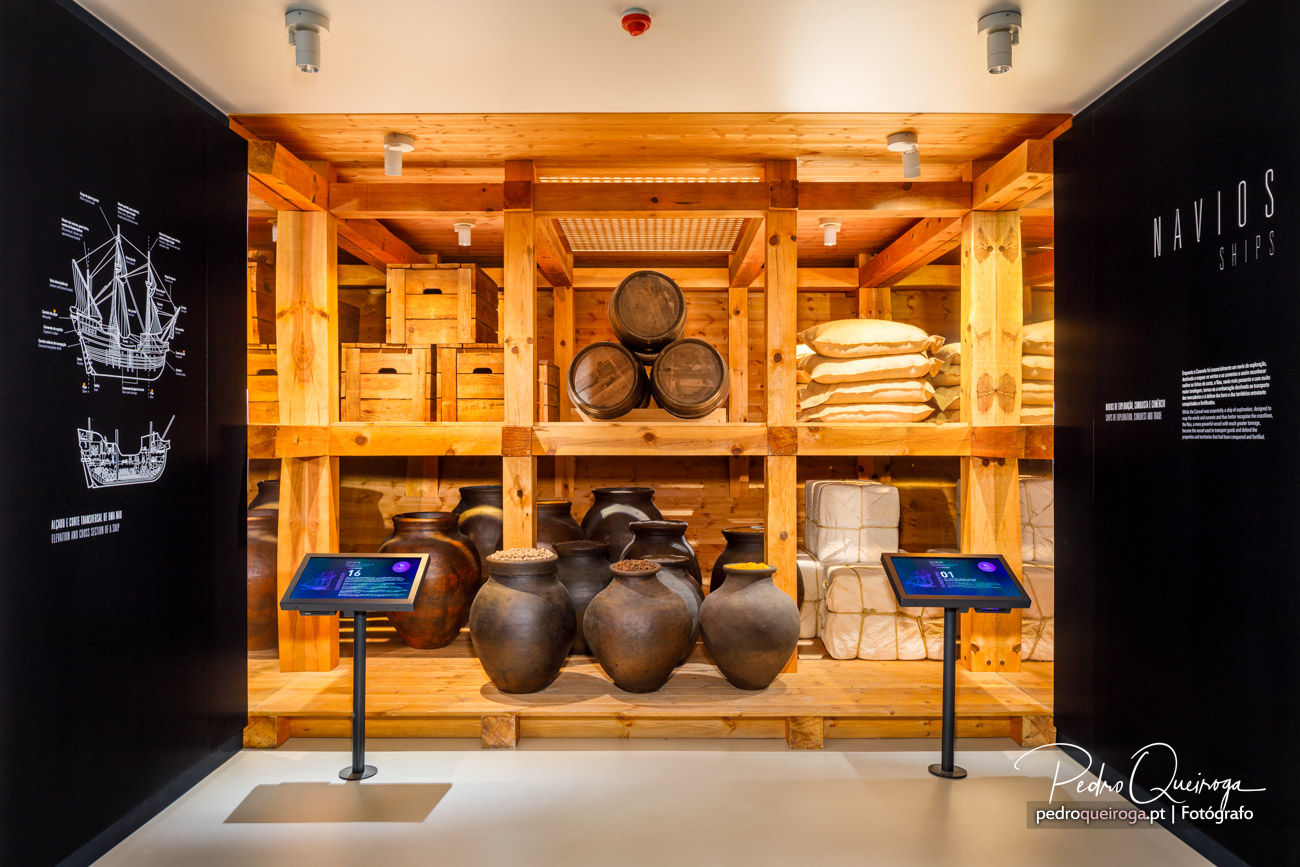 Estrutura expositiva em madeira com tonéis, ânforas de barro, sacos e painéis informativos num museu marítimo