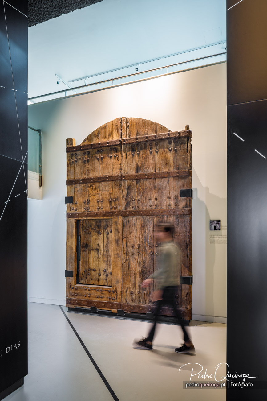 Portão antigo em madeira exposto num museu com visitante em movimento captado com efeito de longa exposição