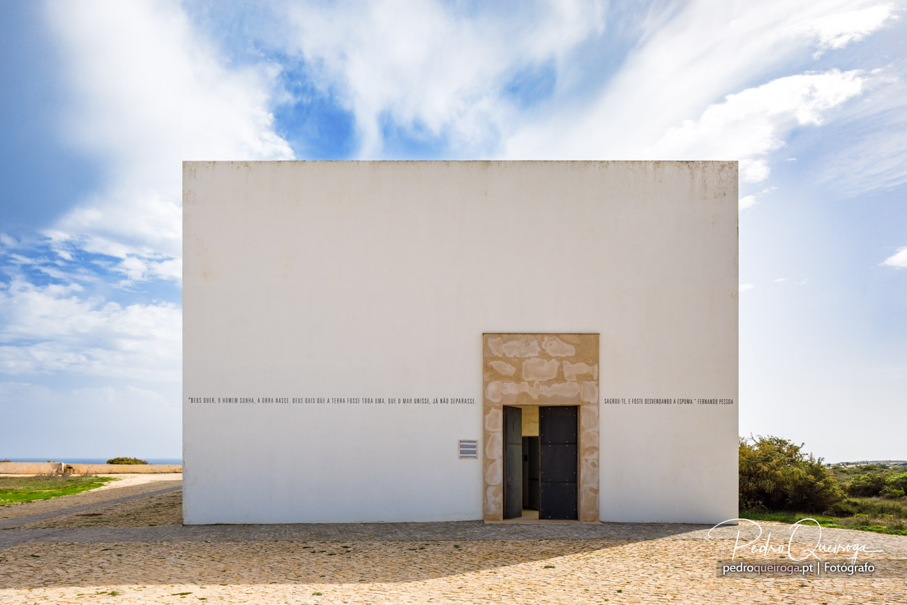 Fachada branca minimalista com porta em pedra e inscrições poéticas, numa composição fotográfica limpa e céu azul