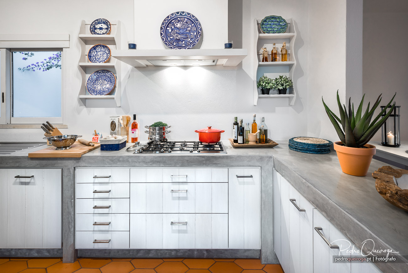 Cozinha moderna com móveis brancos, bancada cinza, pratos azuis decorativos e cacto em vaso terracota à direita