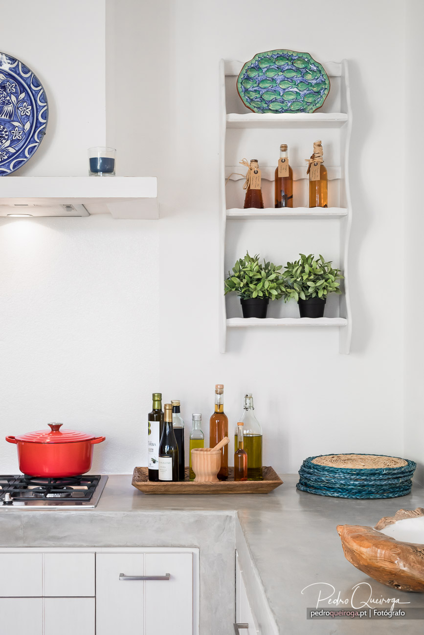 Cozinha moderna com prateleiras decorativas, panela vermelha, óleos aromáticos e detalhes em tons naturais e vibrantes.