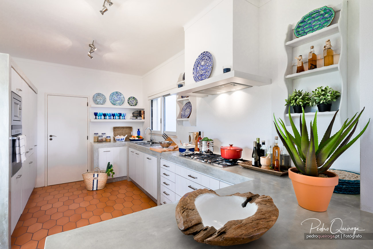 Cozinha branca moderna com pratos decorativos azuis na parede, pavimento terracota e plantas junto à bancada cinza