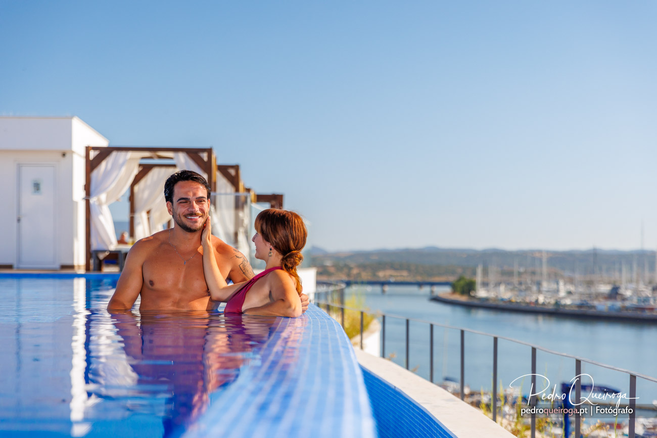 Casal relaxa em piscina infinita com vista mar e gazebos de decoração elegante ao fundo