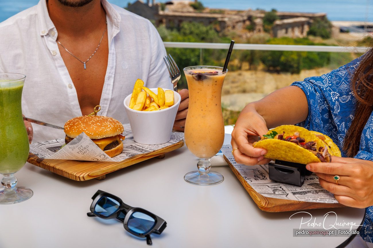 Casal partilha hambúrguer, batatas fritas e tacos numa esplanada ensolarada, fotografia de Pedro Queiroga
