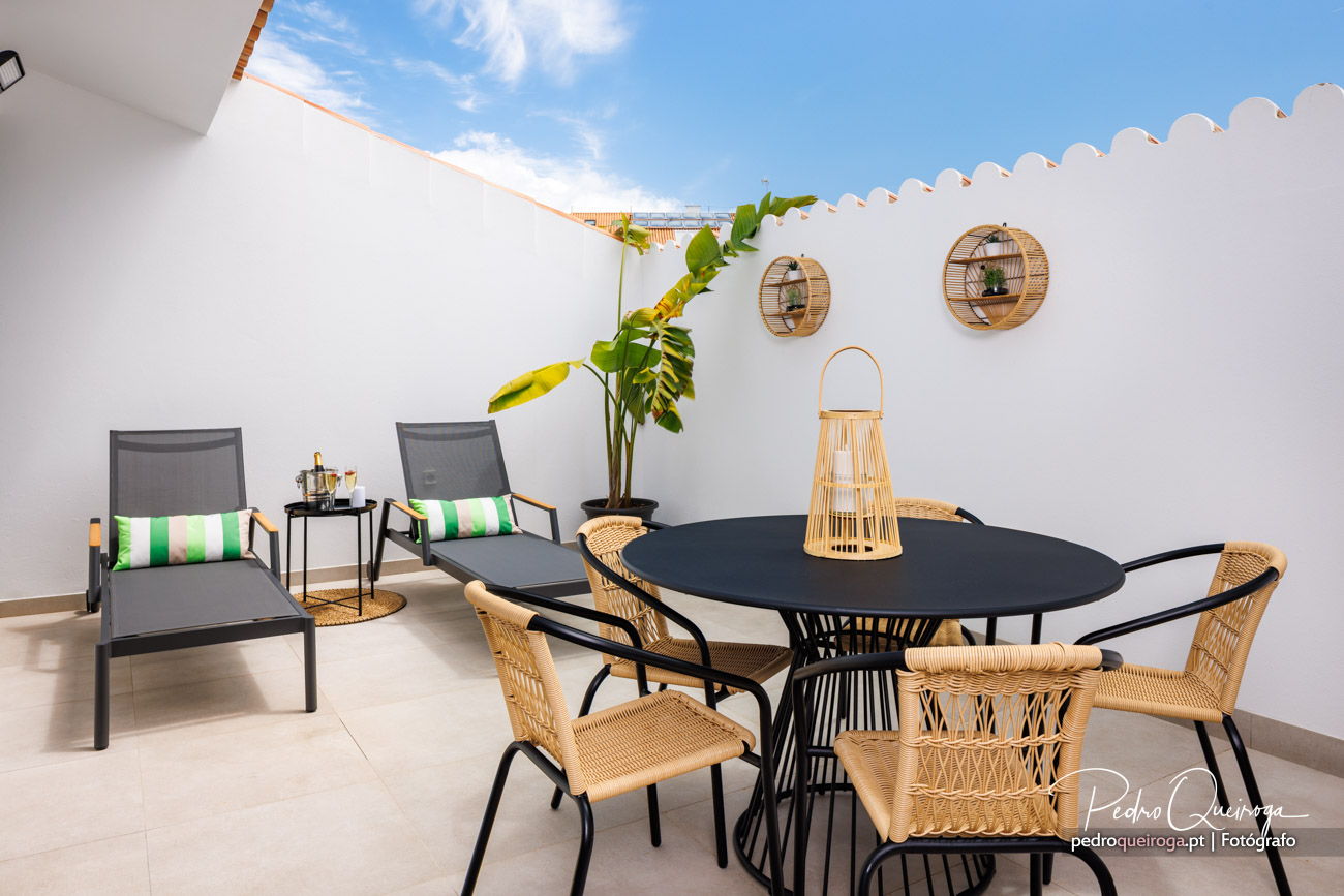 Terraço moderno com mesa preta, cadeiras de vime e espreguiçadeiras, ideal para fotografias de imobiliário