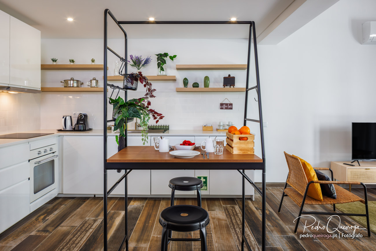 Cozinha moderna com estrutura metálica preta, prateleiras em madeira, plantas decorativas e zona de refeições integrada