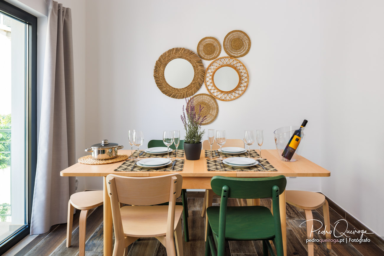 Sala de jantar moderna com mesa em madeira, cadeiras verdes e bege, e parede decorada com espelhos de fibra natural.