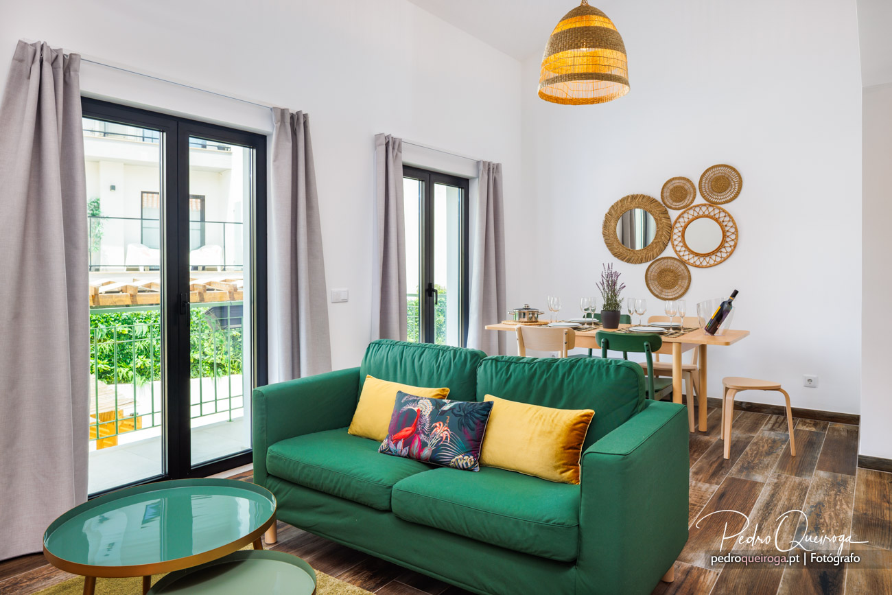 Sala moderna com sofá verde esmeralda, mesa de jantar em madeira e decoração rattan na parede branca