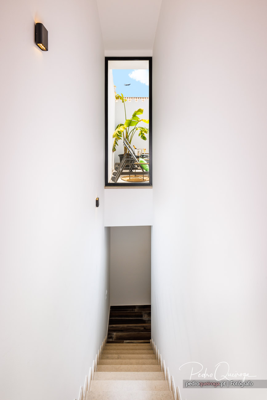 Escada minimalista em tons claros com janela vertical de caixilho preto e aplique moderno na parede branca