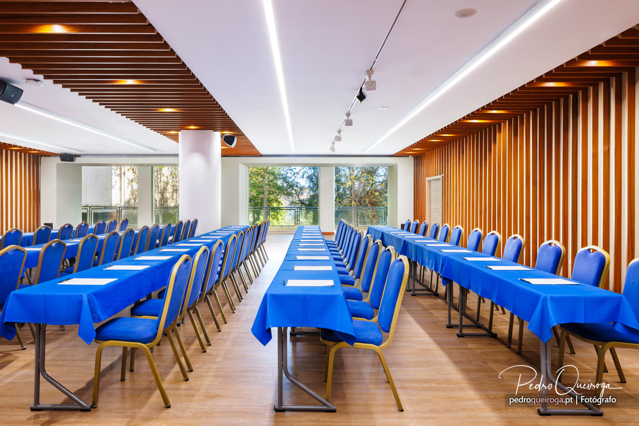 Sala de conferências moderna com mesas e cadeiras azuis, teto em ripado de madeira e iluminação embutida elegante.