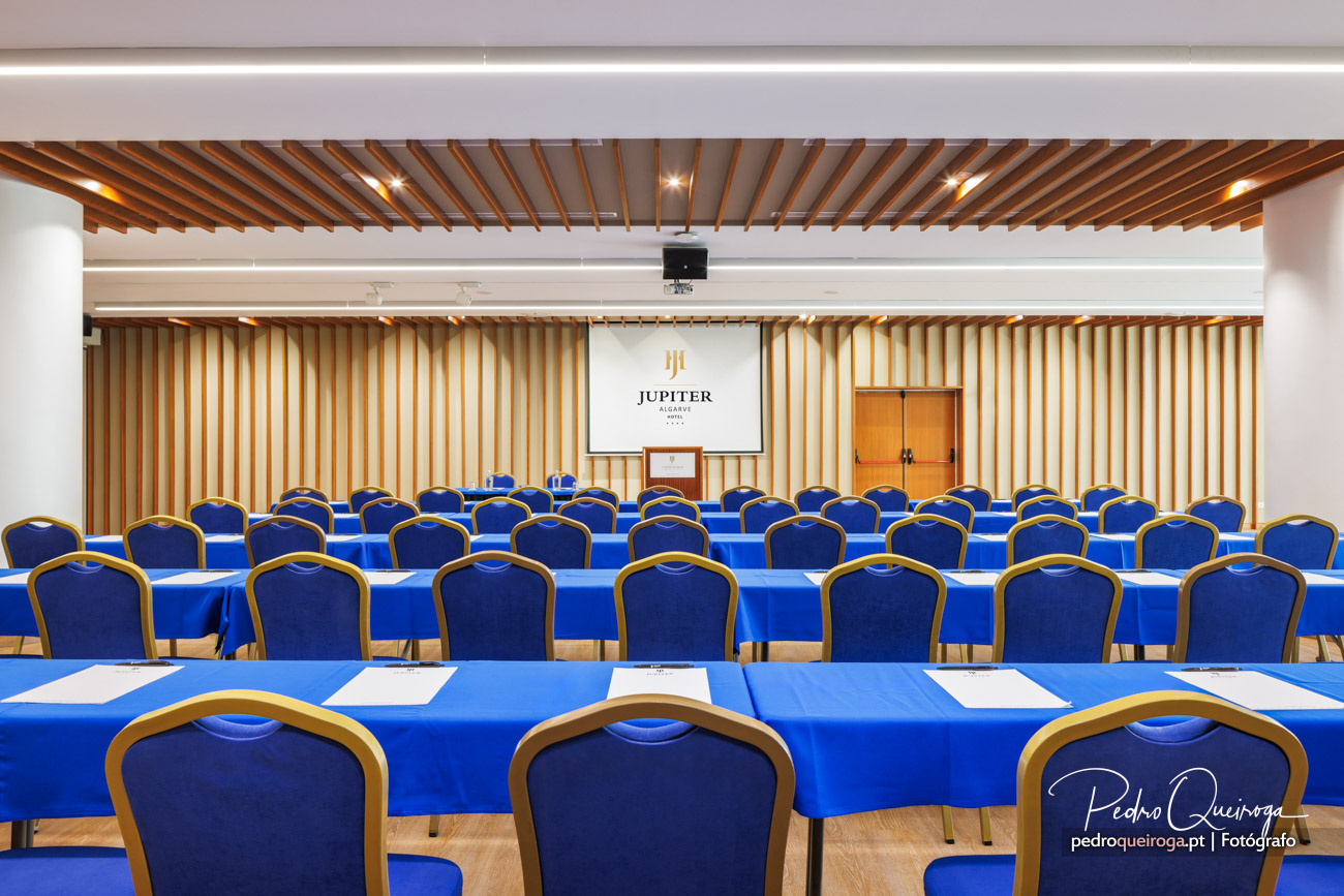 Sala de conferências do Jupiter Algarve Hotel com cadeiras azuis, mesas e projetor central para eventos corporativos