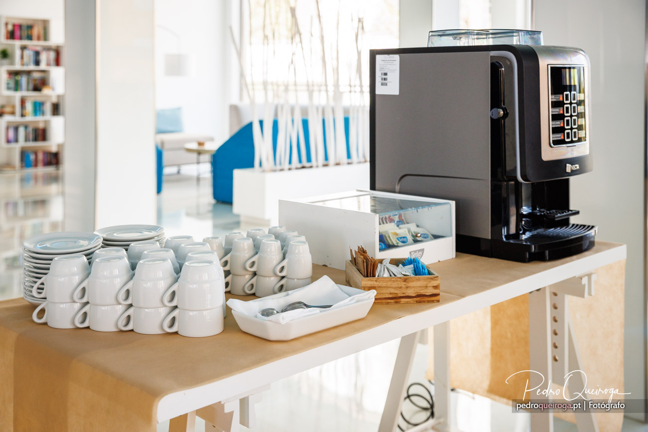Máquina de café profissional preta junto a filas de chávenas brancas organizadas num balcão moderno e luminoso