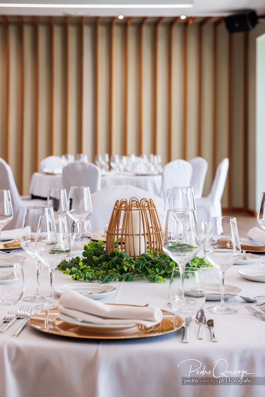 Mesa de jantar elegante com centro decorativo em rattan, folhagens verdes e louça dourada num ambiente luminoso