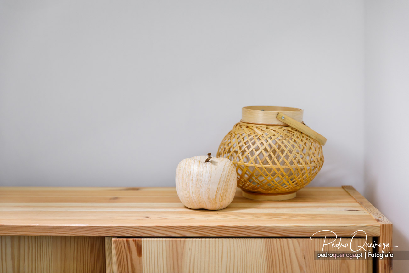 Lanterna de bambu entrançado e maçã decorativa em madeira sobre móvel de pinho com fundo cinza minimalista.