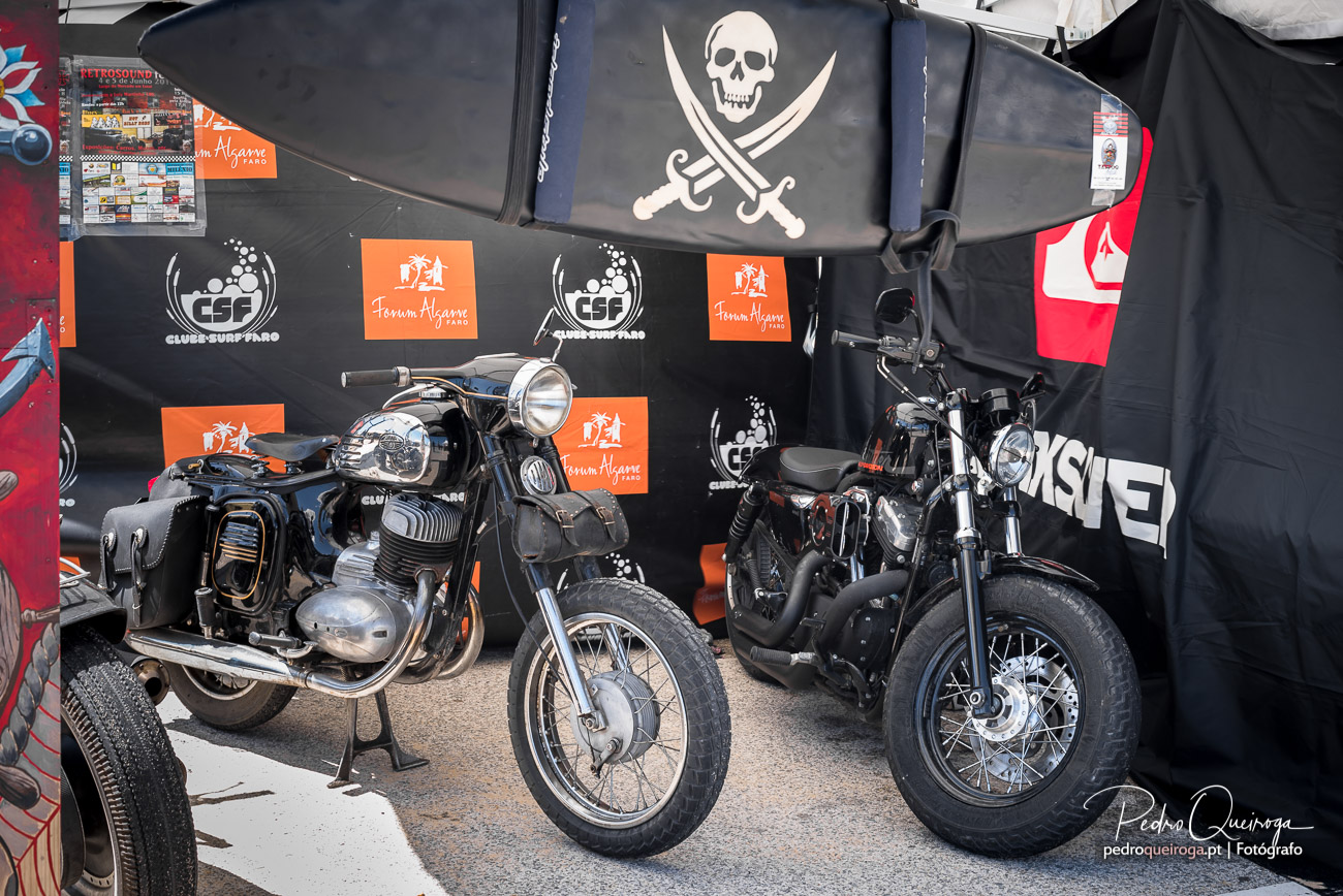 Duas motos clássicas expostas junto a tenda decorada com caveira e espadas cruzadas em evento motard