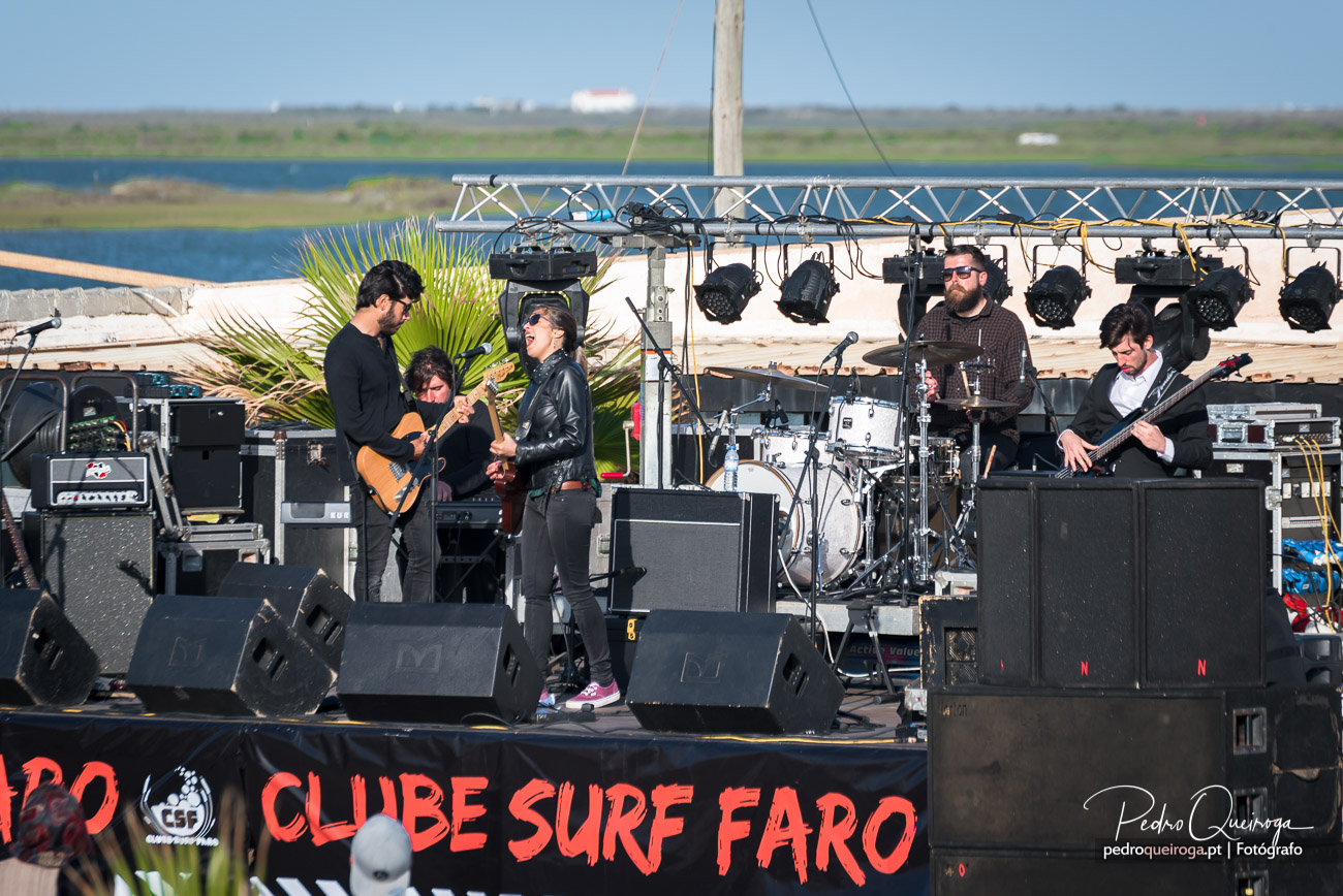 Banda ao vivo no palco do Clube Surf Faro, com composição fotográfica natural e paisagem ribeirinha ao fundo