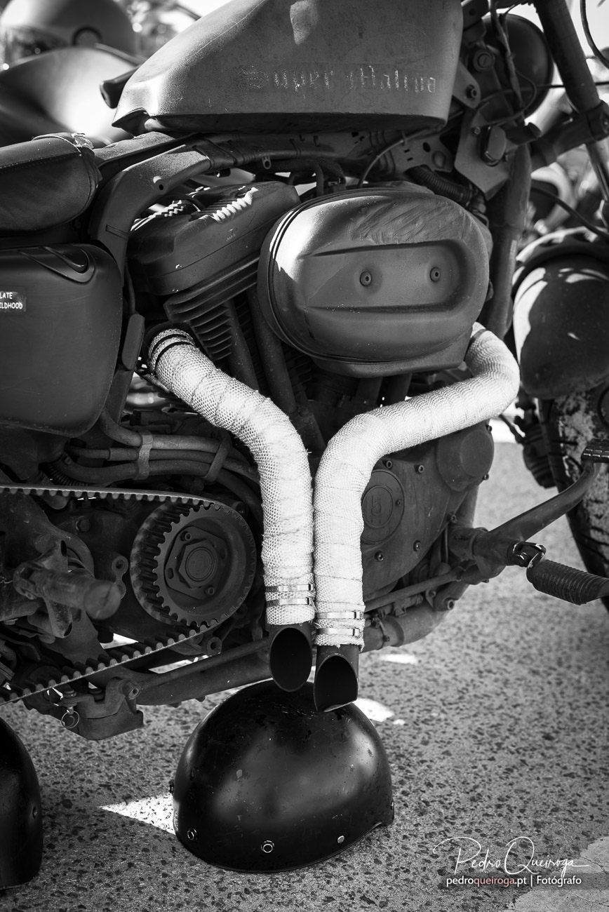 Pormenor do motor de motocicleta com tubagem protegida e correia dentada visível em preto e branco