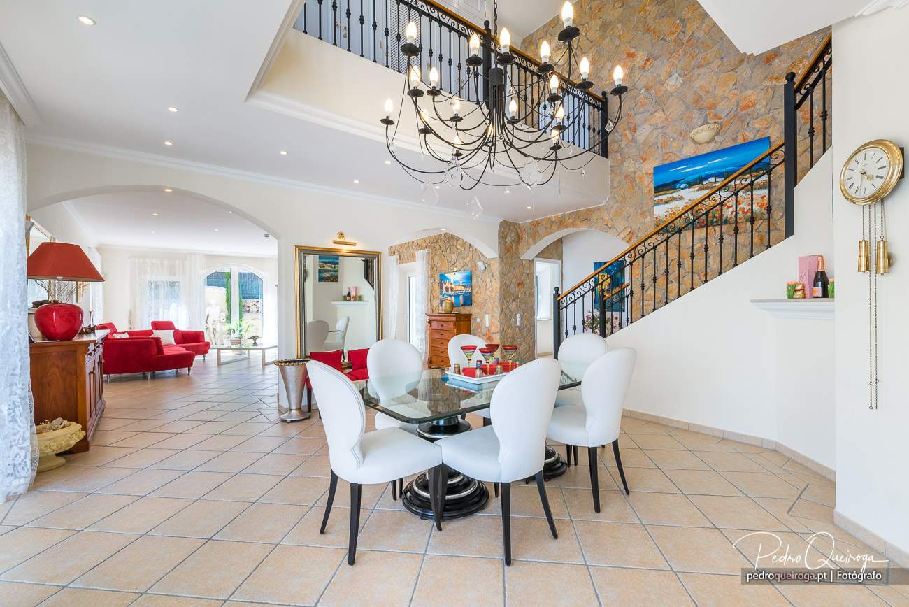 Sala de jantar ampla com escadaria em ferro, candeeiro elegante, parede em pedra e toques de cor vermelha