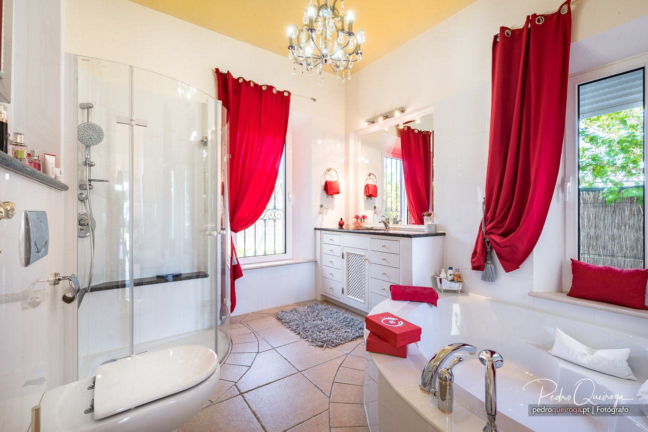 Casa de banho elegante com cortinados vermelhos, candeeiro de cristal e arquitectura de interiores luminosa e ampla.